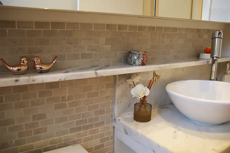 projeto de banheiro com mármore e pastilhas banheiro com bancada, frontão e prateleira em mármore branco, , louças e metais Deca, revestimento em pastilha de mármore em formato de tijolinho