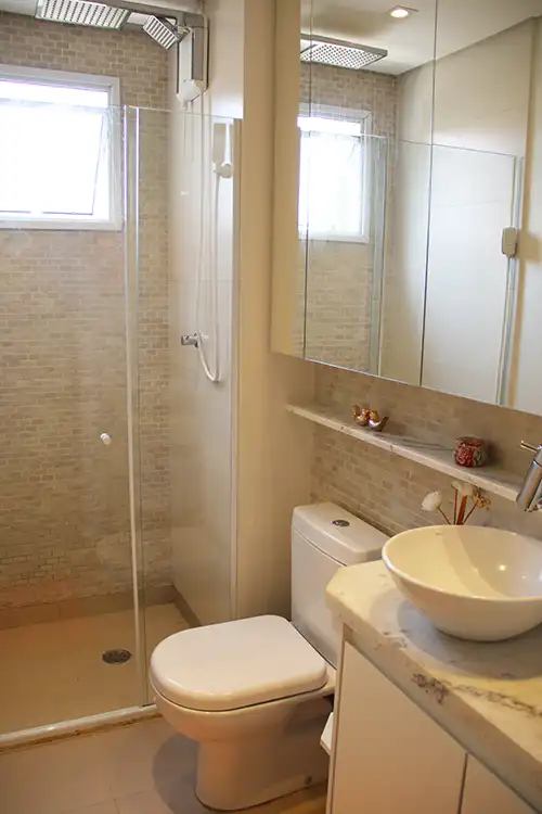 banheiro de apartamento pequeno com armário com espelho, bancada e prateleira em mármore, porcelanato e pastilhas
